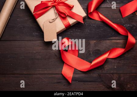 roll of brown kraft packaging paper, red silk ribbon on a brown wooden background Stock Photo