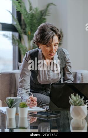 Portrait of mature businesswoman using laptop for online coaching or consultation sitting in an armchair in office. Stock Photo