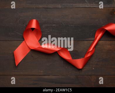 red silk ribbon folded into a loop on a brown wooden background Stock Photo