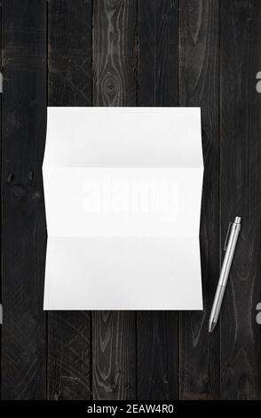 Blank folded White A4 paper sheet mockup and pen on black wood background Stock Photo