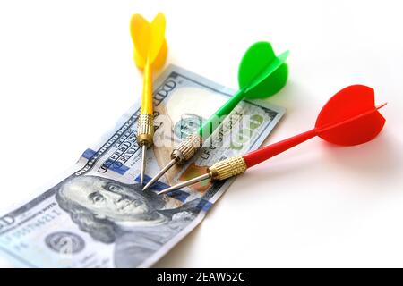 investing with darts in yellow, green and red colors on a white background and 100 US dollars, and dollars for an accurate investment Stock Photo