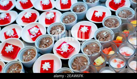 Red jelly dessert with whipped cream served on white plate. Square red jelly in plate on table at restaurant for lunch buffet. Sweet food. Jelly agar. Dessert buffet catering concept, selective focus. Stock Photo