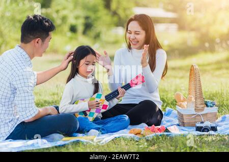 Happy family having fun and enjoying outdoor with playing Ukulele during a picnic Stock Photo