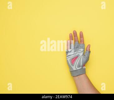 female hand in a gray glove for tributes to sports and driving a bicycle on a yellow background