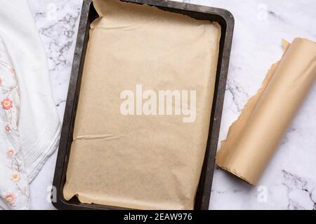 empty rectangular metal baking sheet and roll of brown parchment paper on white background Stock Photo