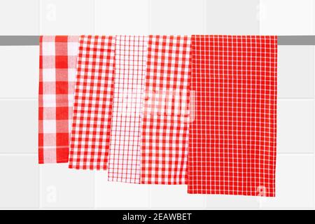 Closeup of various red checkered kitchen towels hang on a clothes rail against blurred bright tile background. Stock Photo