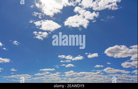 Bright sky background with few small clouds, strong sun shines through creating some lens flares Stock Photo