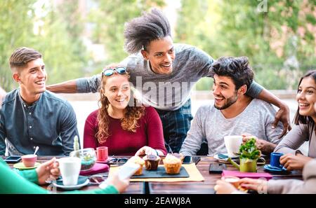 Multiracial friends drinking coffee at bar outdoors - People talking and having genuine fun together at cafeteria garden - Friendship concept Stock Photo