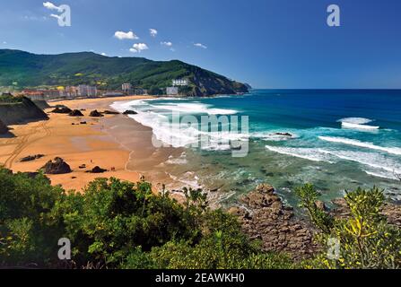 View of sand beach with blue ocean and white waves surrounded by green hills Stock Photo
