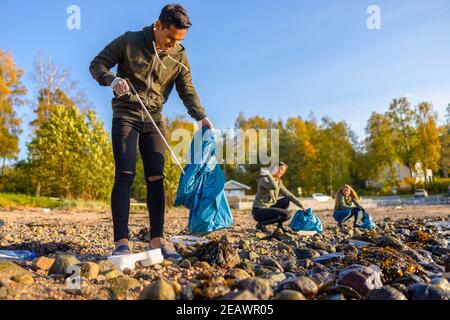 Focused man cleaning beach with group of volunteers on sunny day Stock Photo