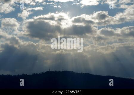 Mountain called Uetliberg on the horizon of Zurich. Sun rays are penetrating through clouds covering the sun creating irregular pattern above. Stock Photo