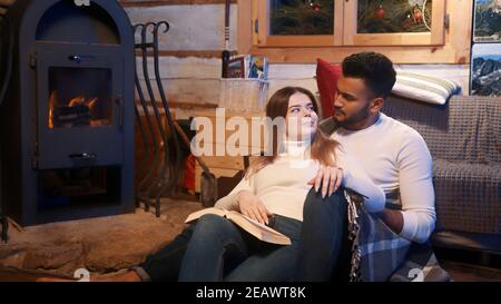 Happy young couple relaxing and reading book together near the fireplace. Winter holidays, christmas or valentines day. High quality photo Stock Photo