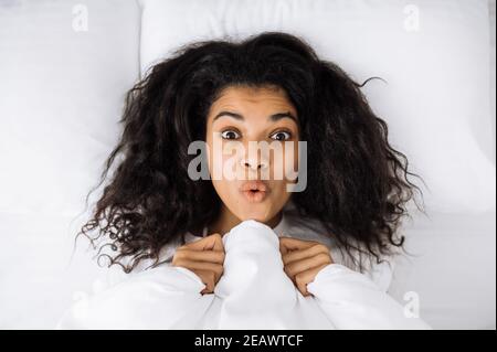 African american young woman lay in bed, posing, making funny faces. Happy female relaxing in bed, after good night sleep. Beautiful girl waking up, f Stock Photo