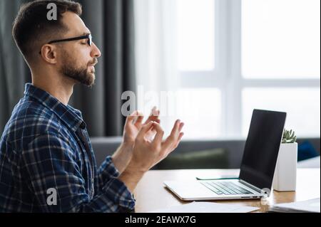 Satisfied caucasian busy freelancer is meditate at the workplace. Calm male employee takes a break from work online. Distant work or learning Stock Photo