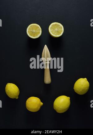 Whole lemons, halves of lemons and  wooden squeezer on black background Stock Photo