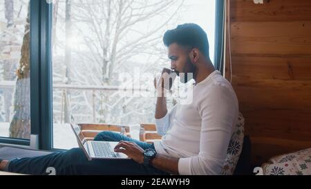 Young man browsing social media and drinking tea near the window on winter vacation. High quality photo Stock Photo