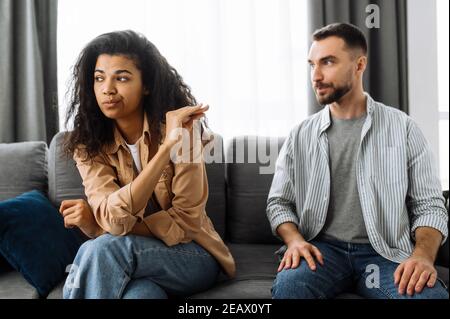 A married couple finds out the relationship, a quarrel between lovers. Multiracial couple in love quarreling at home on couch over household or financ Stock Photo
