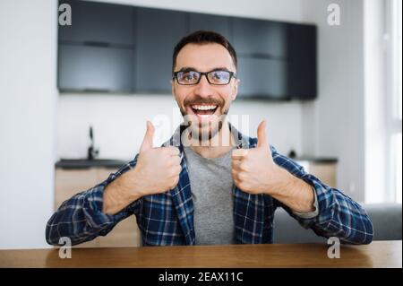 Portrait of a friendly caucasian student or freelancer guy during video call, he looks at the camera, smiling and and gesturing with hands showing thu Stock Photo