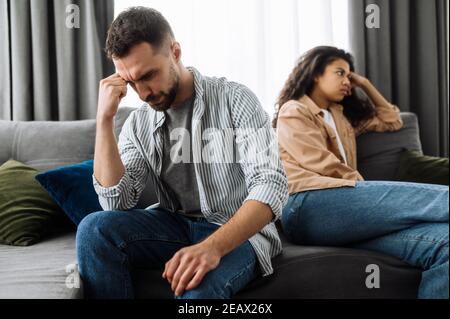 Quarrel between a couple in love. An upset guy and a girl are offended and ignore each other while sitting on the couch, turning away in different dir Stock Photo