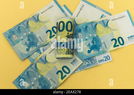 background of twenty euro banknotes on yellow color and a roll of banknotes held by a rubber band concept economy savings Stock Photo