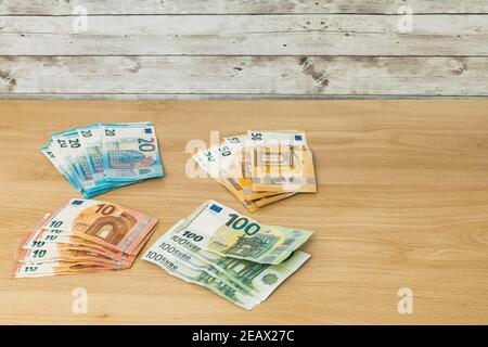 Several stacks of euro banknotes grouped by value of ten twenty fifty and one hundred on a wooden table finance and savings concept Stock Photo