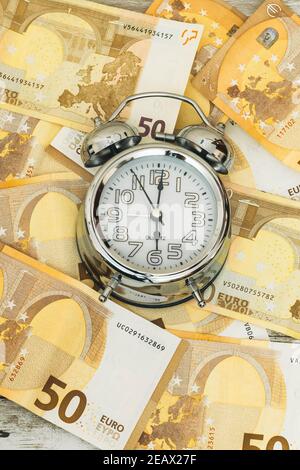 detail of an analog clock on a background of euro banknotes in concept of time is money with a vertical picture Stock Photo