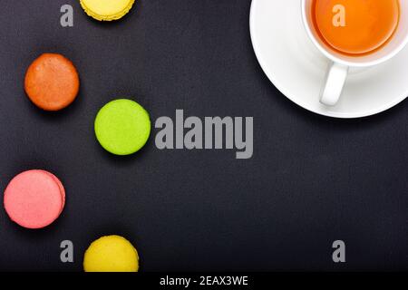 Multicolored macaroon cookies and a cup of tea on a black background. Stock Photo