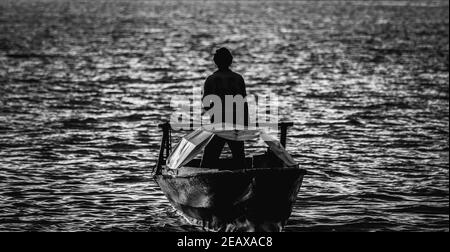 Grayscale shot of a man standing on a boat sailing in the sea Stock Photo