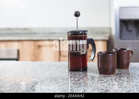 French press with fresh coffee next to two mugs on a modern kitchen counter. No people in the making. Selective focus Stock Photo