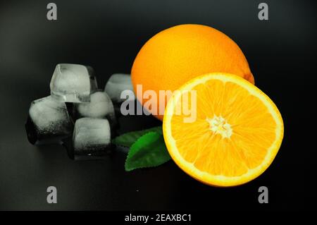 Two ripe oranges with leaves and pieces of melted ice lie on a black background. Close-up. Stock Photo