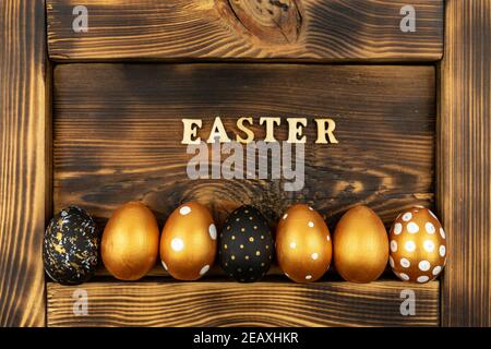 Easter festive background. Top view of easter eggs colored with golden paint and inscription in English Easter. Wooden letters on dark wood background Stock Photo