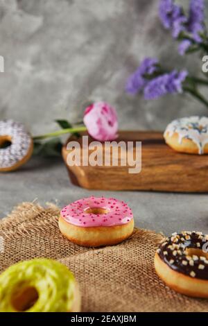 Multicolored donuts with glaze and sprinkles with flowers on a gray background. Stock Photo