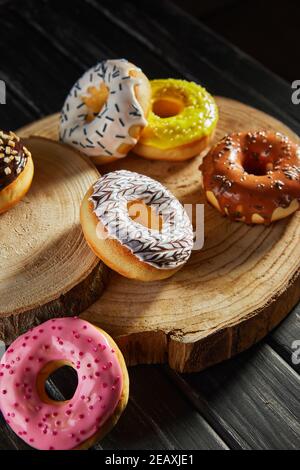 Multicolored donuts with glaze and sprinkles on wooden coasters on a black background. Stock Photo