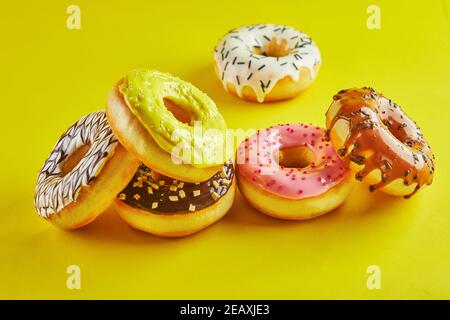 Multicolored donuts with glaze and sprinkles on yellow background. Stock Photo