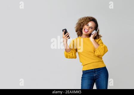 Attractive African American woman wearing headphone and happily listening to music from her smartphone isolated on gray studio background with copy sp Stock Photo