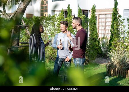 Group of multicultural friends enjoying chatting and drinking alcohol on their weekend outdoors at the backyard Stock Photo