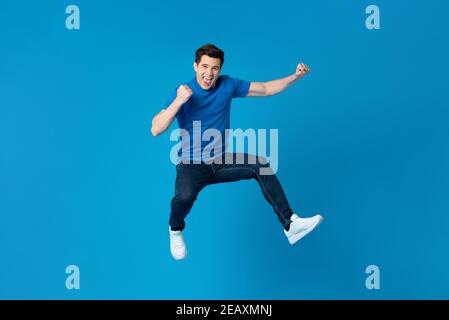 Smiling handsome American man joyfully jumping and raising his fists isolated on blue studio background  fro success and freedom concepts Stock Photo