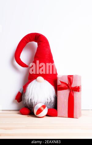 Santa gnome and homemade christmas gift. Festive christmas decoration with elf . Handmade decor with funny dwarf in red cap. Greeting card. Stock Photo