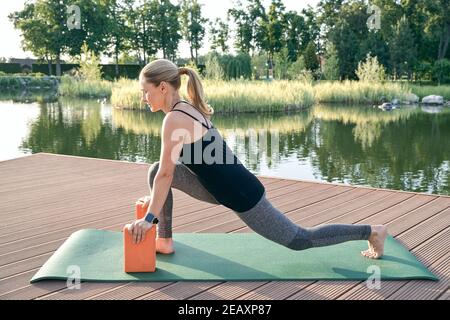 Keep your body healthy. Sporty attractive woman in sportswear using yoga blocks or bricks while doing yoga on a mat in nature on a sunny day Stock Photo