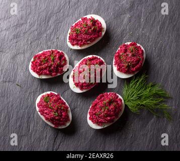 Stuffed eggs with beetroot with cream cheese, garlic and spicy herbs on a black slate background, top view. delicious homemade food Stock Photo