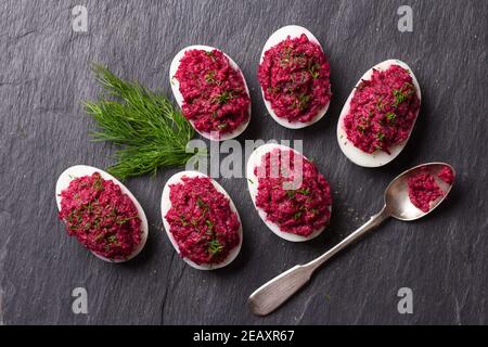 Stuffed eggs with beetroot with cream cheese, garlic and spicy herbs on a black slate background, top view. delicious homemade food Stock Photo