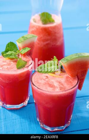 Closeup of fresh smoothie juice in two glasses and half filled jar with watermelon slices and mint leaves Stock Photo