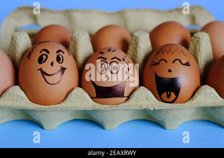 Creative Easter eggs with Corona virus (COVID19) protection concepts. Chicken eggs with doodle faces wearing medical masks and toy rabbit on blue. Stock Photo