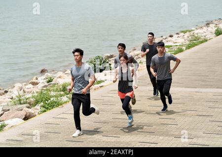 group of five young asian adults running outdoors in seaside park Stock Photo
