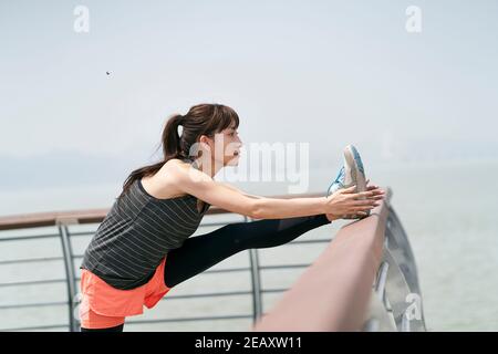 young asian woman in sportswear stretching legs outdoors in seaside park Stock Photo