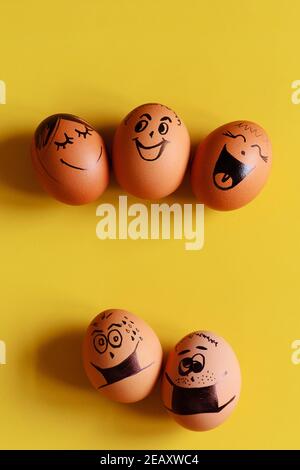 Creative Easter eggs with Corona virus (COVID19) protection concept. Diverse chicken eggs with doodle faces wearing medical masks on yellow background Stock Photo