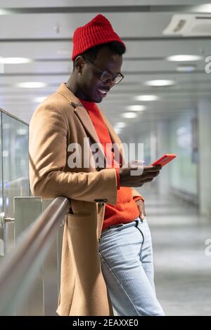 Smiling African American hipster man using cellphone, chatting in social networks, typing message. Stock Photo