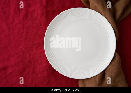 Clean empty white plate, fork and knife on bright linen red cranberry textile tablecloth on table Stock Photo