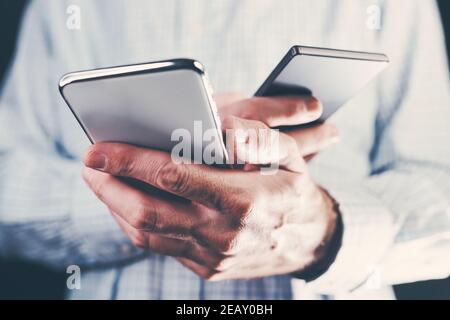 Data transfer between two mobile phones, adult male holding two smartphones Stock Photo