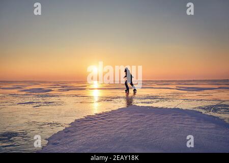 Man ice skating in silhouette at frozen lake against beautiful orange sunrise Stock Photo